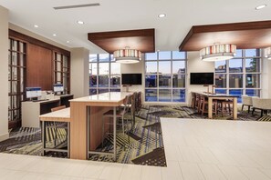 A modern hotel lobby with a reception desk, seating area, and large windows offering views of the outside.