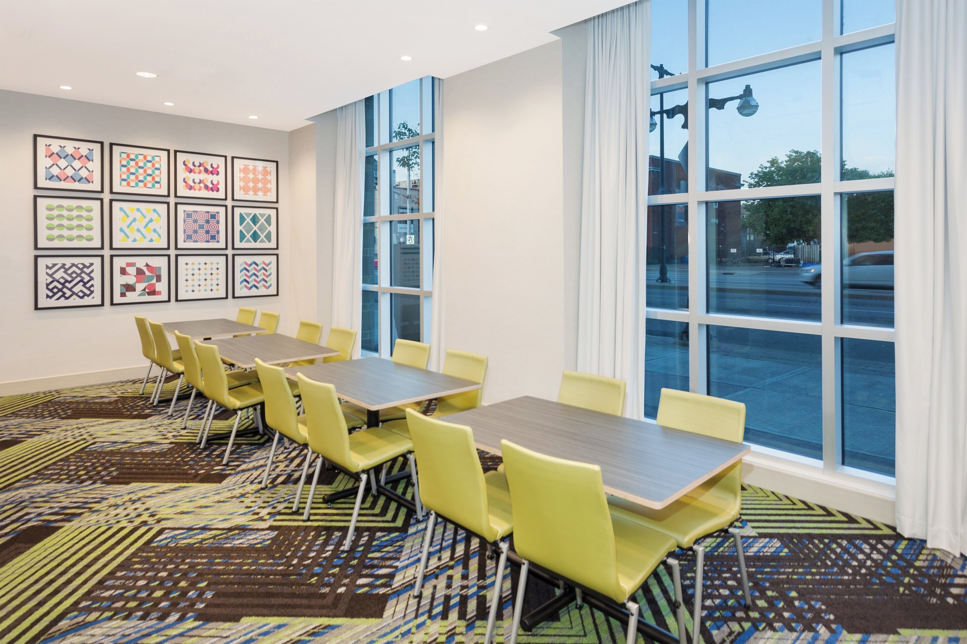 Une salle de conférence équipée de tables et de chaises, dotée de grandes fenêtres et ornée de motifs décoratifs sur les murs.