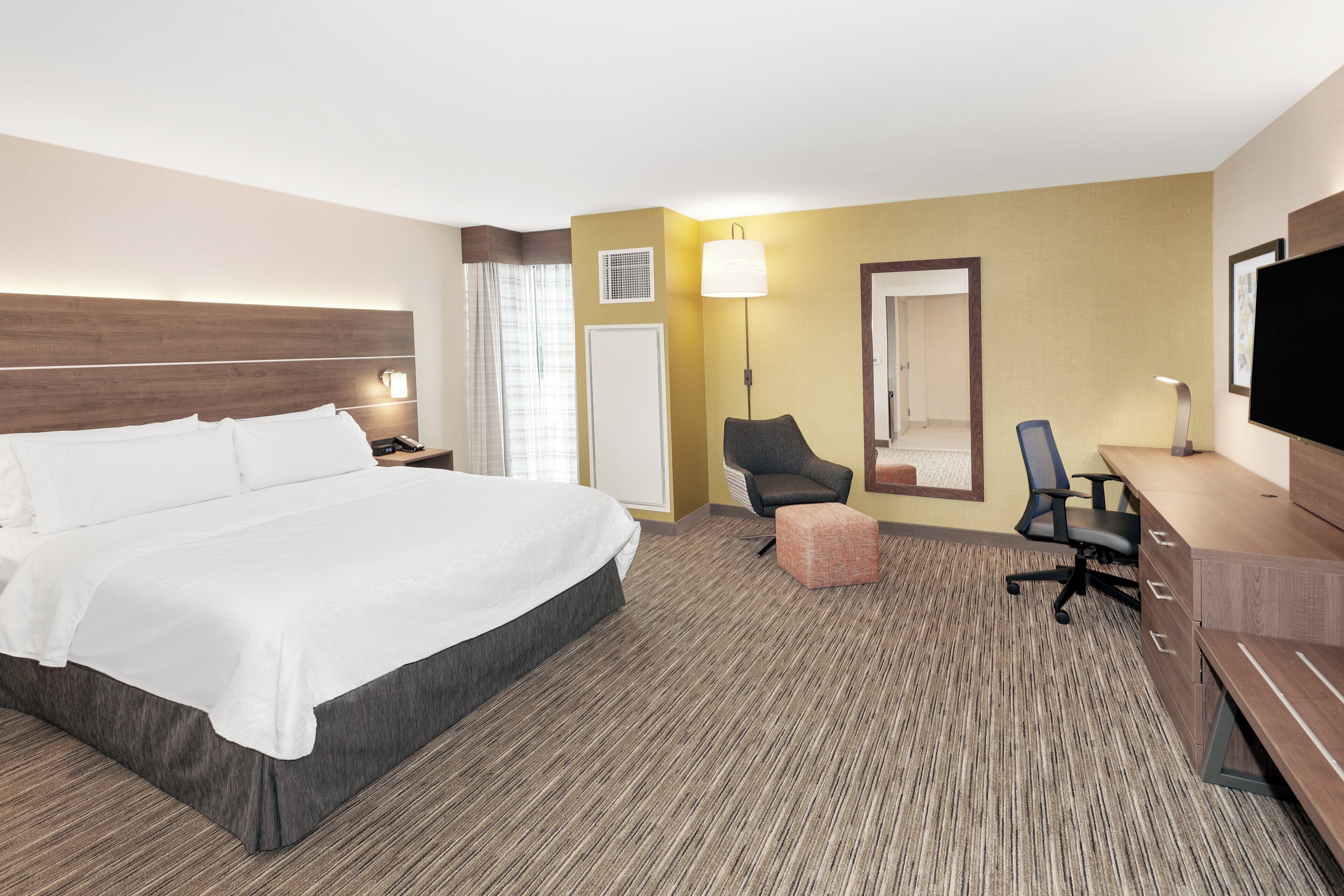 Ein Hotelzimmer mit einem großen Bett, einem Schreibtisch mit Stuhl, einem Fernseher und einer Lampe.
