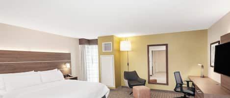A hotel room with a large bed, a desk with a chair, a television, and a lamp.