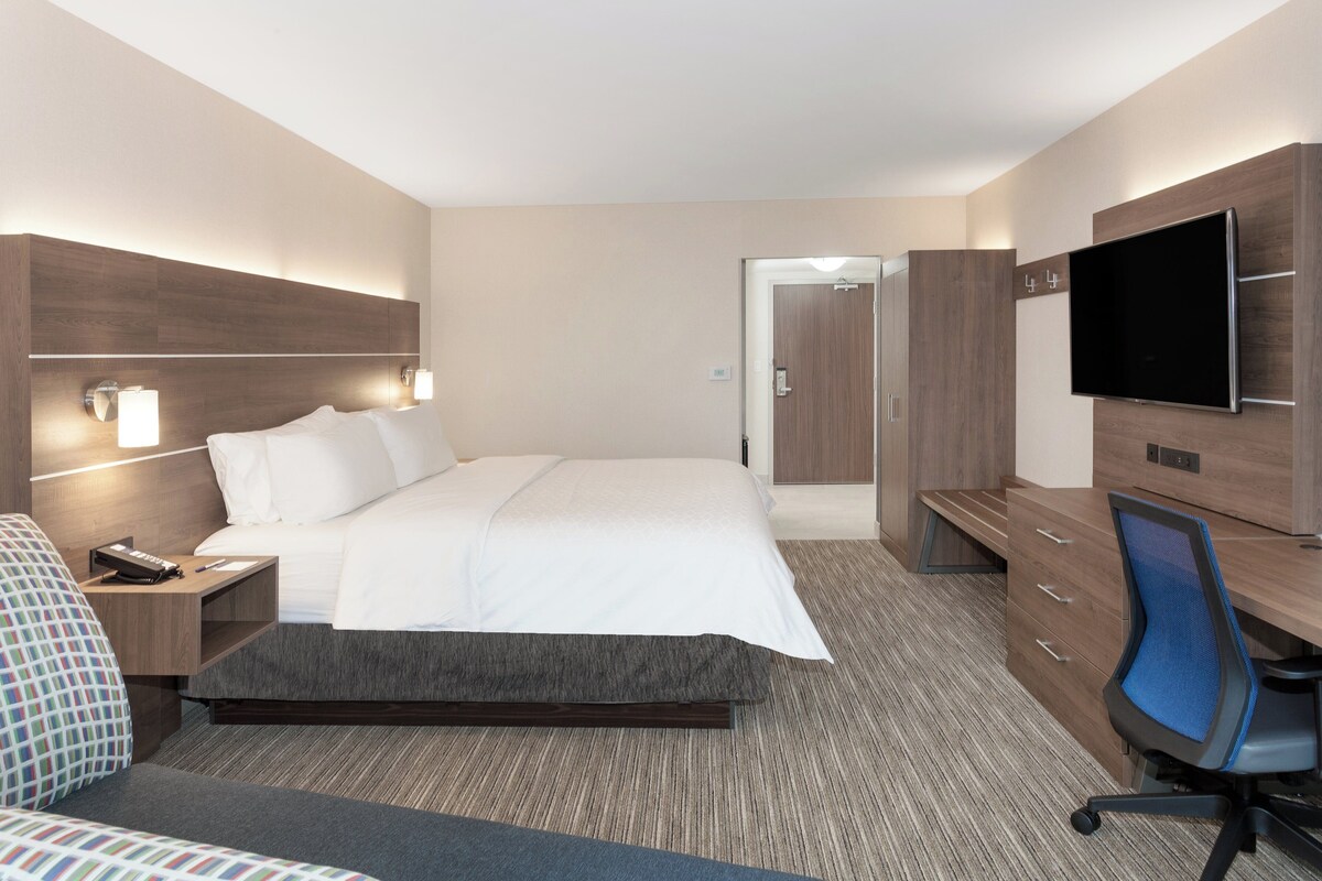 A hotel room with a bed, bedside tables, a desk with a chair, a television, and a wardrobe.