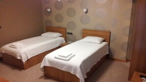 A hotel room with two single beds, each with a white bedspread and pillows, and a small bedside table with a lamp. - Basoglu Bulancak Otel (Bulancak)