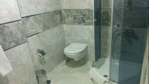 A bathroom with a toilet, a bidet, and a glass-enclosed shower area. - Basoglu Bulancak Otel (Bulancak)