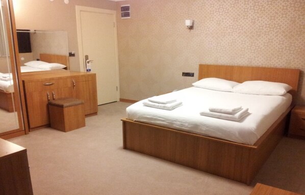 A hotel room with a wooden bed, a wooden dresser, a mirror, and a small bedside table.