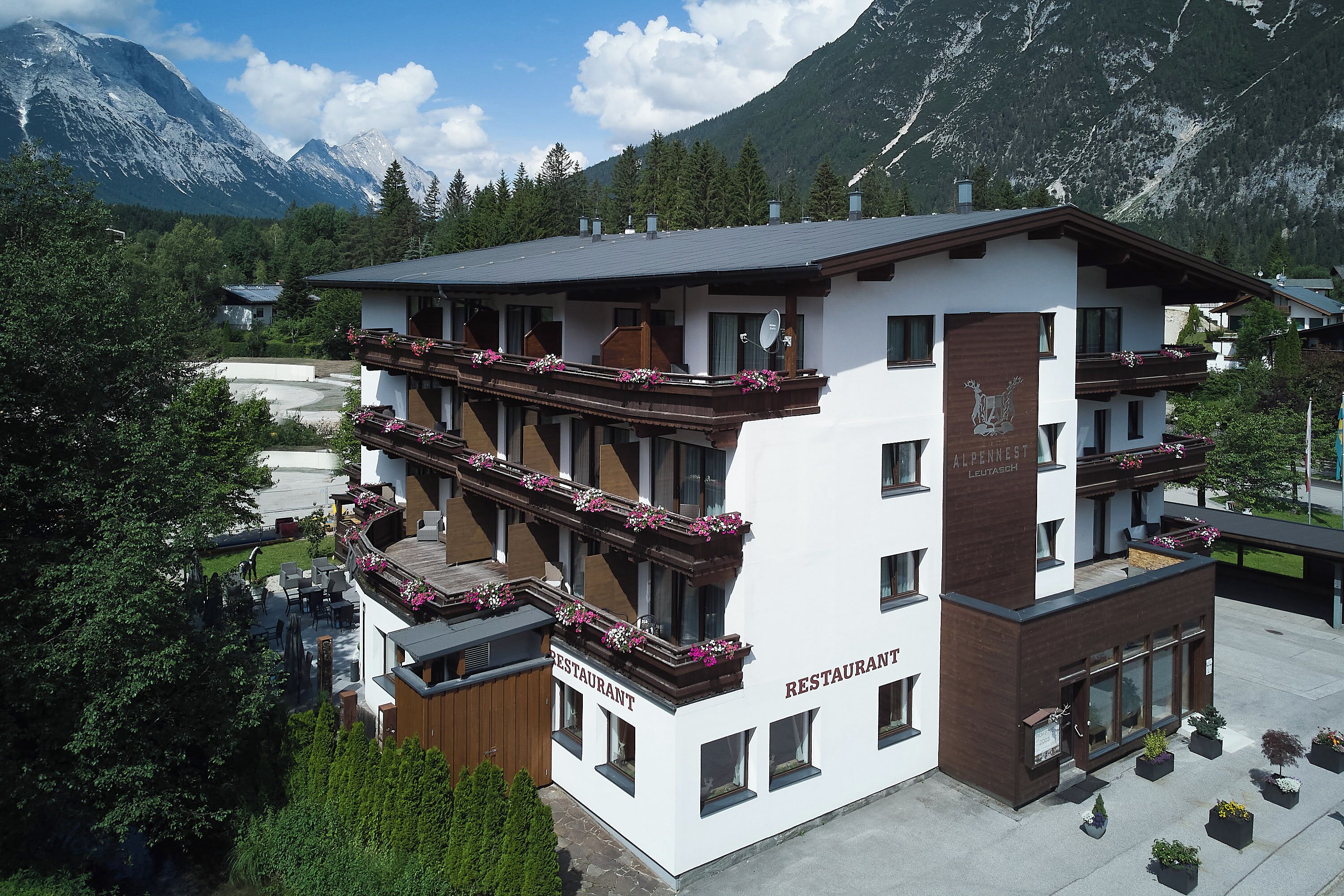 A multi-story building with balconies adorned with flowers, a sign indicating it's a restaurant, and a mountainous backdrop.