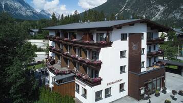A multi-story building with balconies adorned with flowers, a sign indicating it's a restaurant, and a mountainous backdrop.