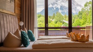 Et hotelværelse med seng, puder, en træsenggavl, et vindue med udsigt til et bjerg og en balkon.