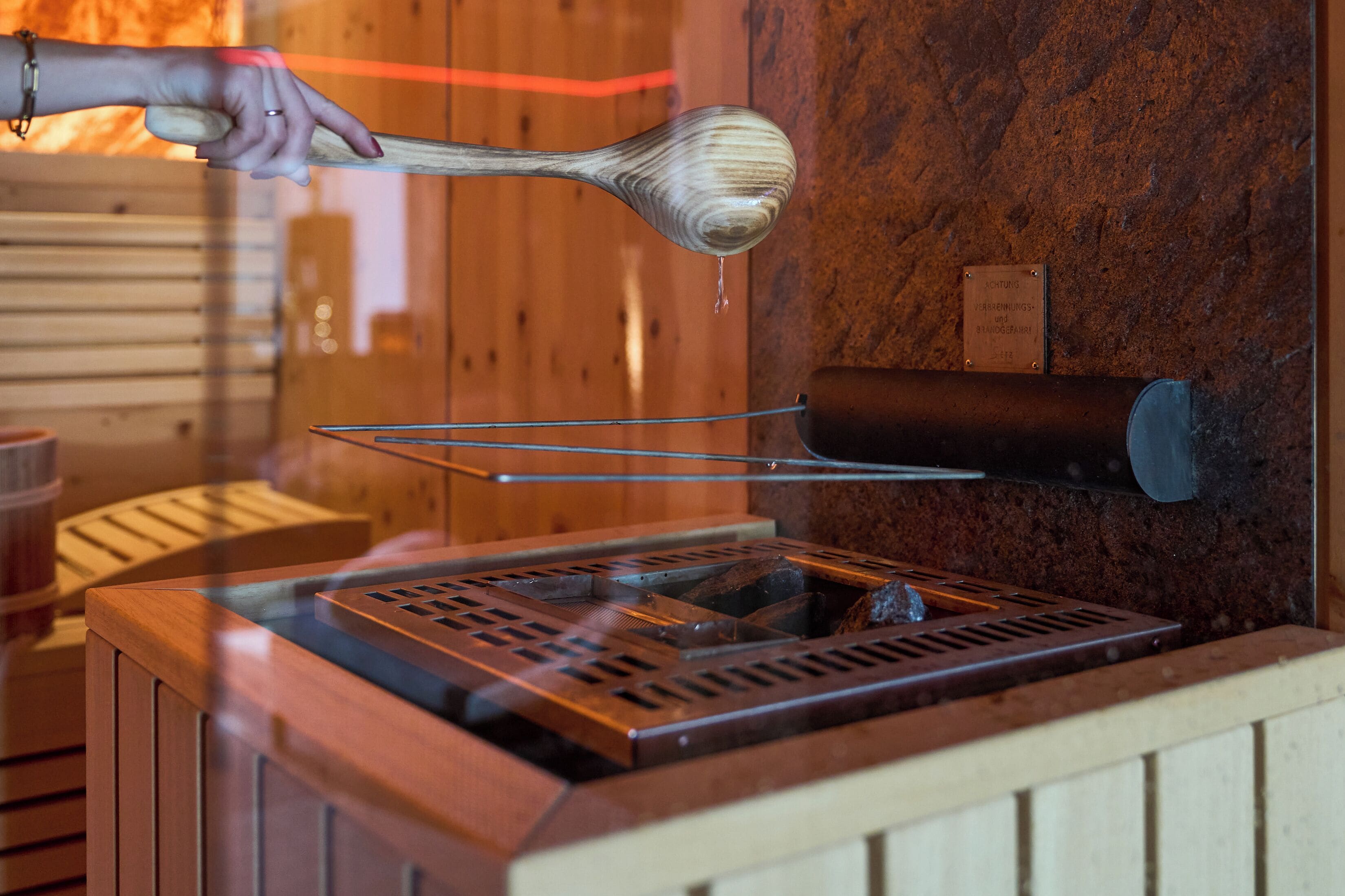 A wooden spoon with a liquid dripping from it, placed on a metal rack above a stove.