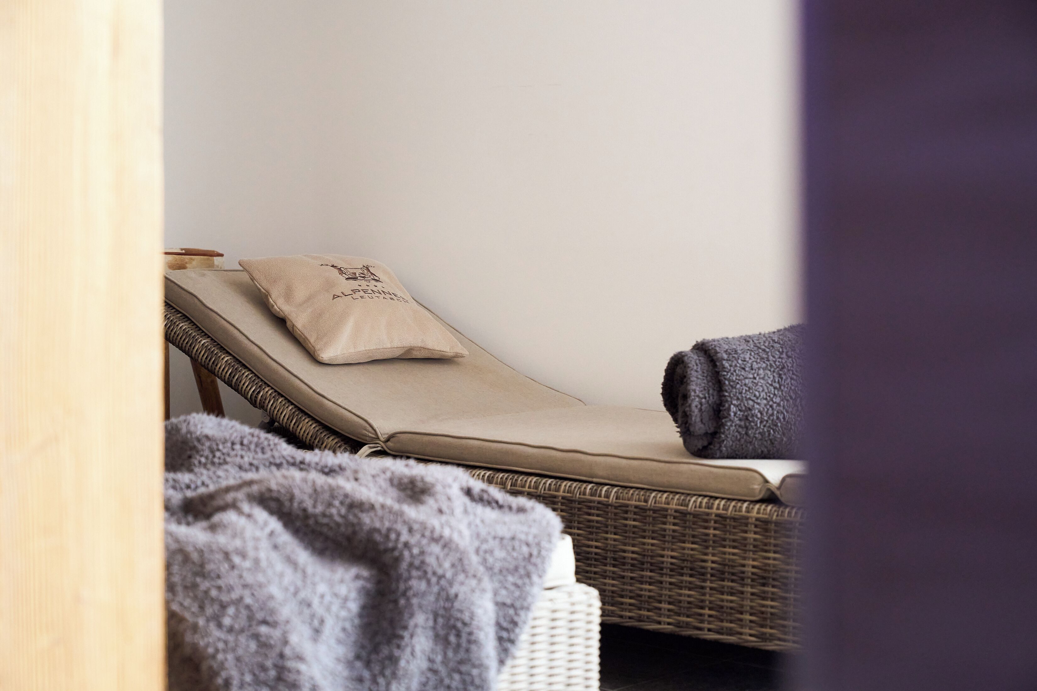 Une salle de spa avec un fauteuil en osier, un coussin beige et une serviette enroulée.