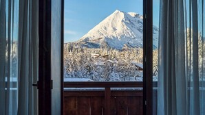 Udsigt fra et værelse med en træbalkon, over et sneklædt bjerg og træer.