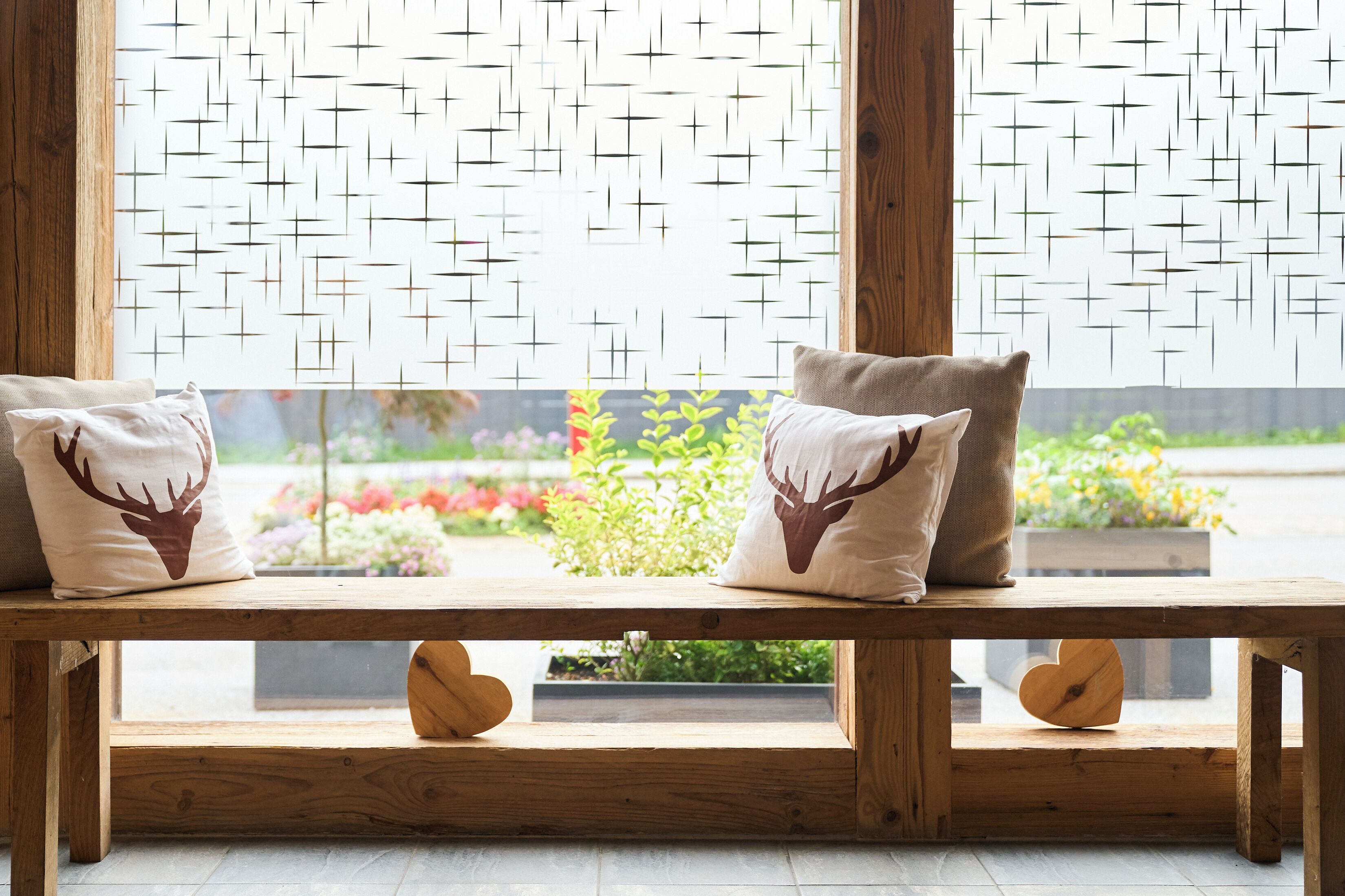 Un banc en bois avec deux coussins, dont l’un est orné d’un motif de cerf, et une fenêtre à motifs géométriques.