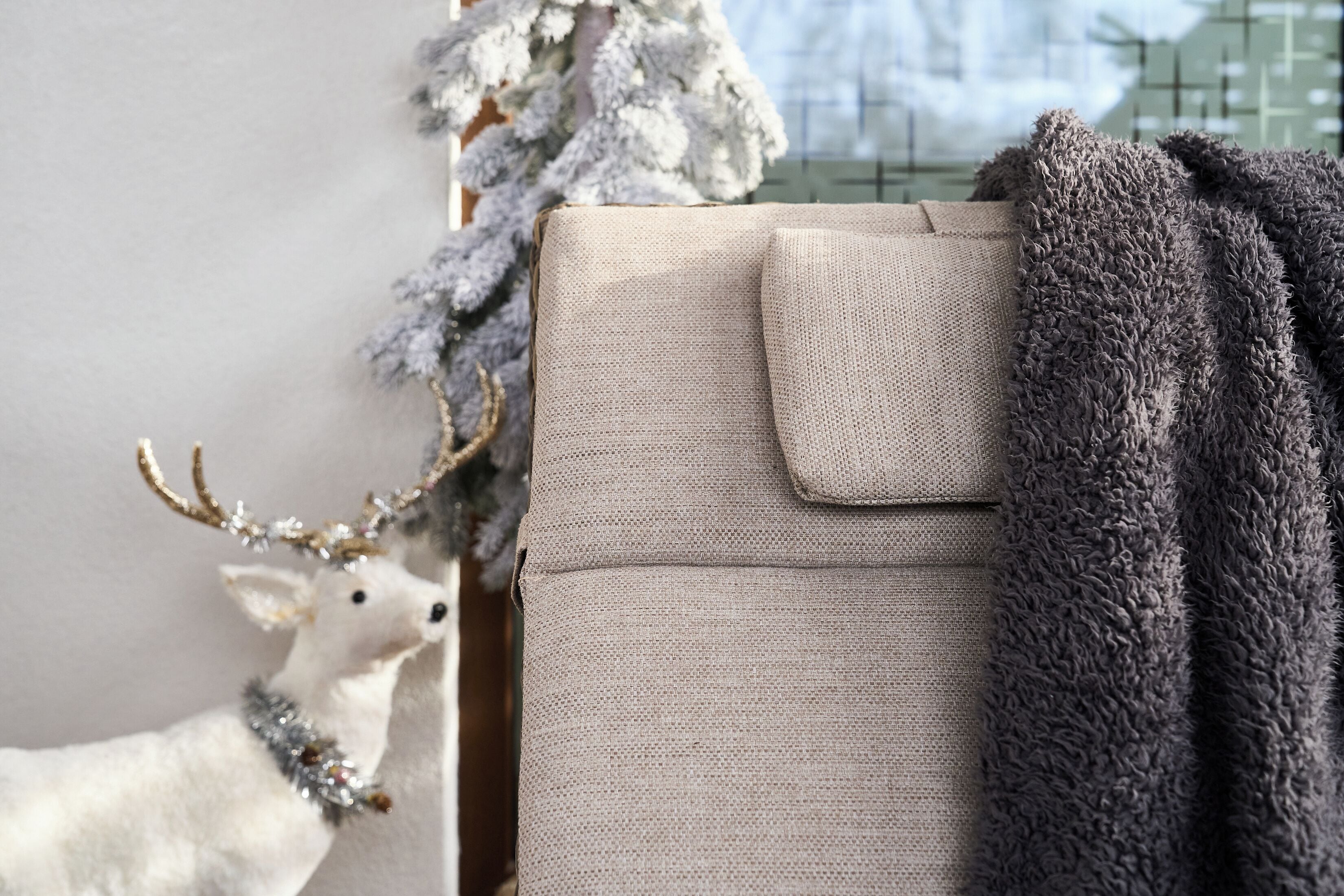 A cozy room with a plush gray sofa, a decorative reindeer, and a frosted Christmas tree.