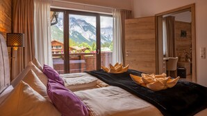 Et hotelværelse med et stort vindue der viser udsigt til et bjerglandskab, et træloft og en seng med puder og et tæppe.