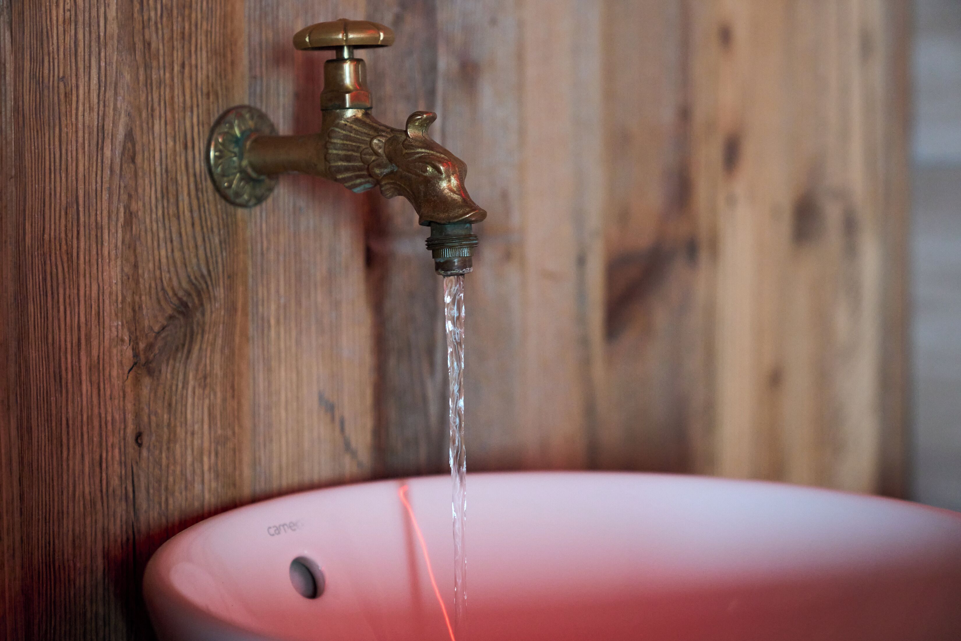 Un grifo de bronce con agua corriendo hacia un lavabo rosa.