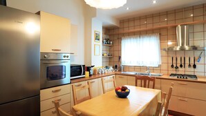 A kitchen with a Bosch refrigerator, microwave, and oven. There is a dining table with chairs and a bowl of fruit. The kitchen has wooden cabinets and a window with curtains. - Bari Primo Piano (Bari)