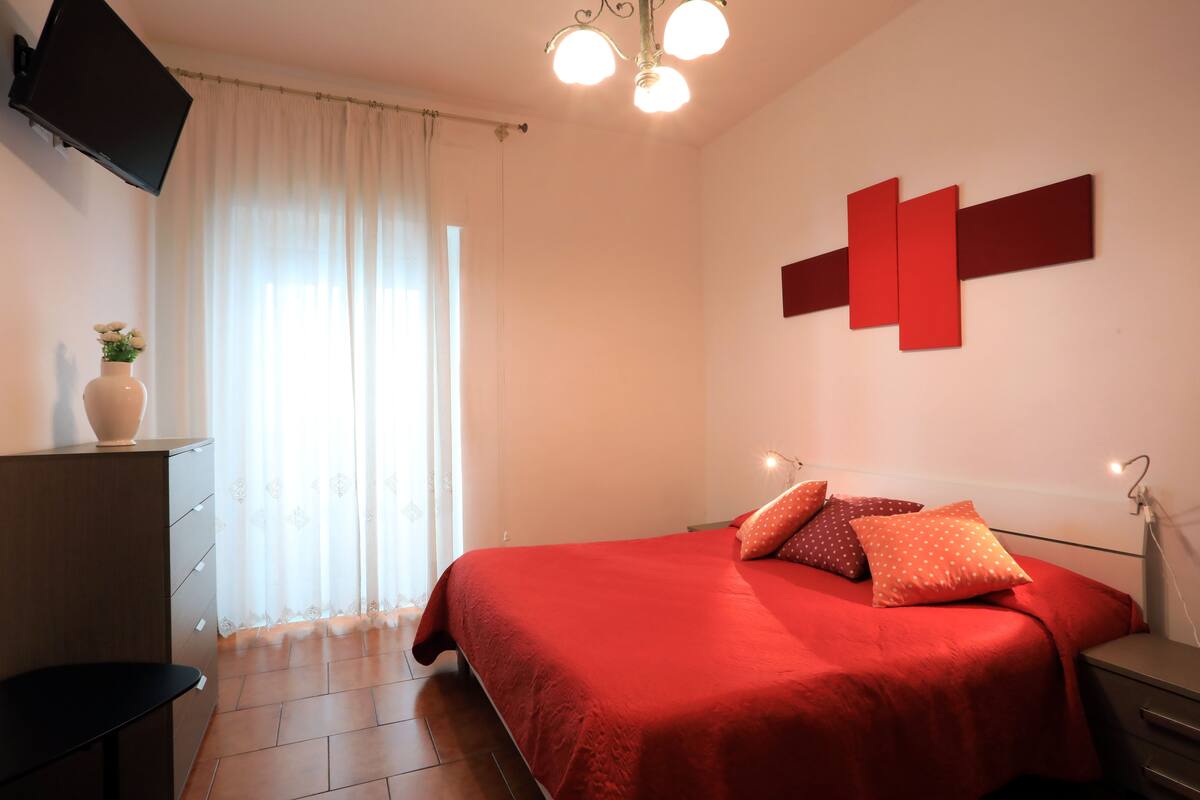 Un dormitorio con cama, escritorio, silla, televisor y ventana con cortinas.