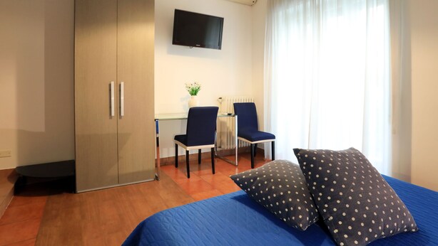 A bedroom with a bed, two chairs, a desk, and a TV. - Bari Primo Piano (Bari)