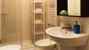 A bathroom with a glass-enclosed shower, a white sink, a toilet, and a towel rack with folded towels. - Bari Primo Piano (Bari)