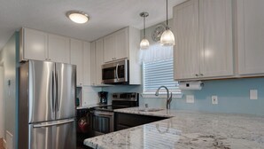 Una cocina moderna con electrodomésticos de acero inoxidable, armarios blancos, encimera de mármol e iluminación colgante.