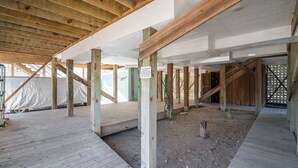 A covered wooden deck area with a sandy floor, wooden beams, and a sign on one of the posts.