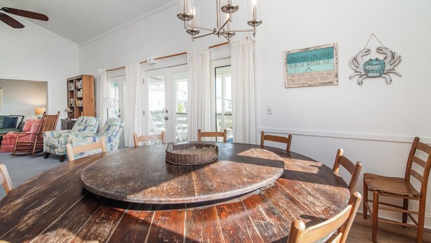 A dining area with a round wooden table, chairs, a chandelier, and a bookshelf.