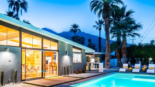 Una casa moderna con piscina, porte vetrate che conducono a una sala da pranzo e palme sullo sfondo.