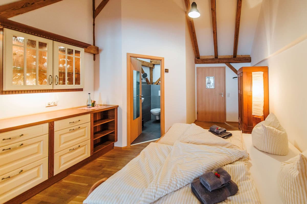Een slaapkamer met een houten bed, een nachtkastje, een kledingkast, en een badkamer die door een open deur zichtbaar is.