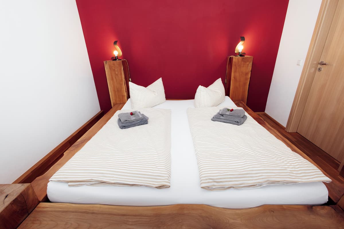 Een tweepersoonsbed met gestreept beddengoed, twee nachtkastjes met lampen, en een rode accentmuur.