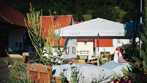 A bed with a checkered blanket, surrounded by flowers and a wooden fence. - Alte Kass Hotel und Kaffeehaus (Neidlingen)