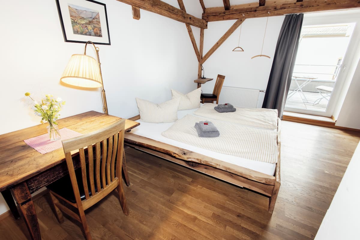Een slaapkamer met een houten bedframe, een bureau met een lamp en een raam met uitzicht.