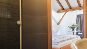 A bedroom with a wooden ceiling, a bed, a small table with a plant, and a window with curtains. - Alte Kass Hotel und Kaffeehaus (Neidlingen)