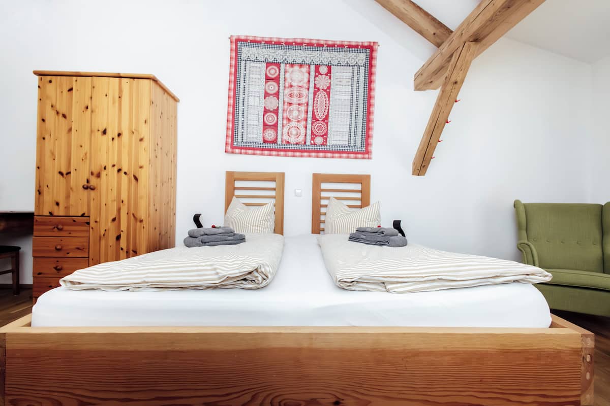 Een slaapkamer met een houten bed, twee nachtkastjes, een groene stoel en een houten kledingkast.