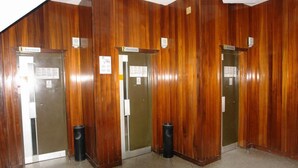 A set of three wooden-paneled doors labeled "Ascensor" with accompanying trash bins.