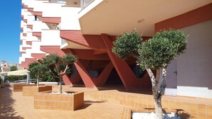 A modern building with a unique architectural design, featuring a series of balconies and a tiled courtyard with small trees and planters.