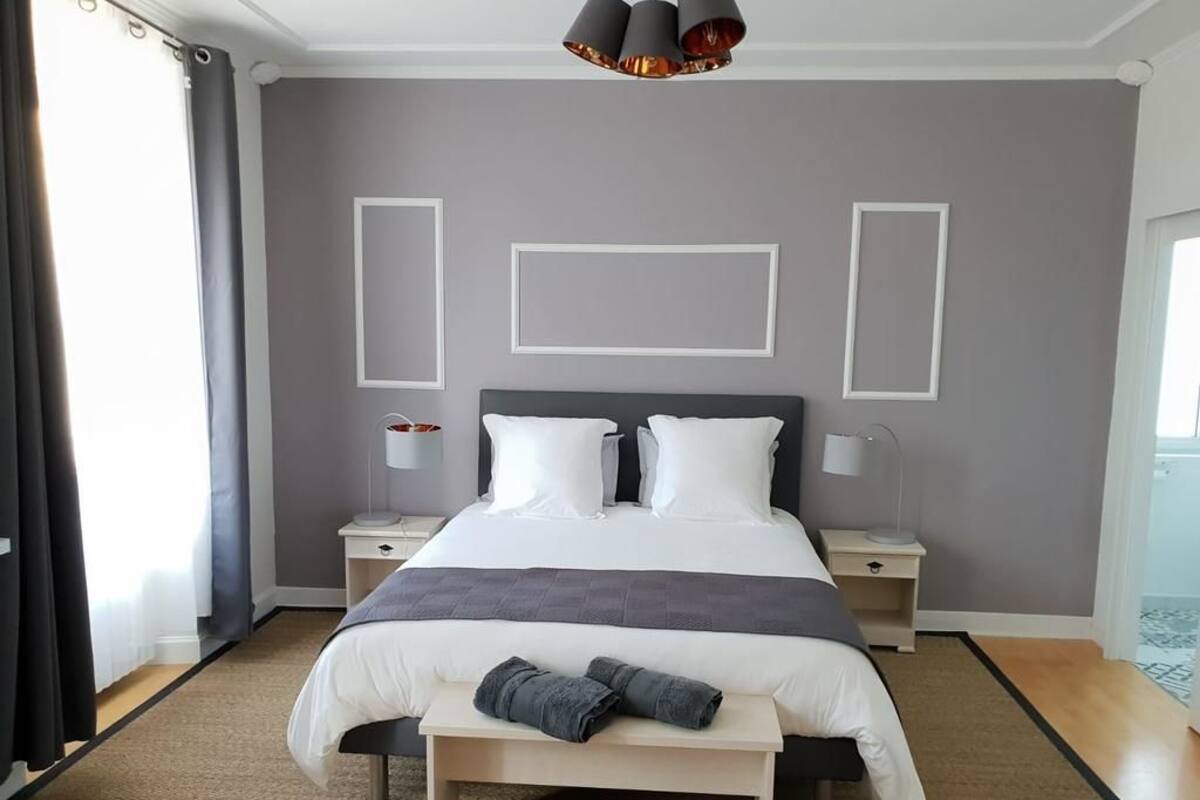Una habitación de hotel moderna con una cama grande, mesitas de noche, un banco y una lámpara de techo.