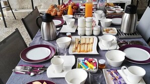 Een ontbijttafel gedekt met borden, bekers en bestek, plus croissants, sinaasappelsap en diverse andere ontbijtspullen.
