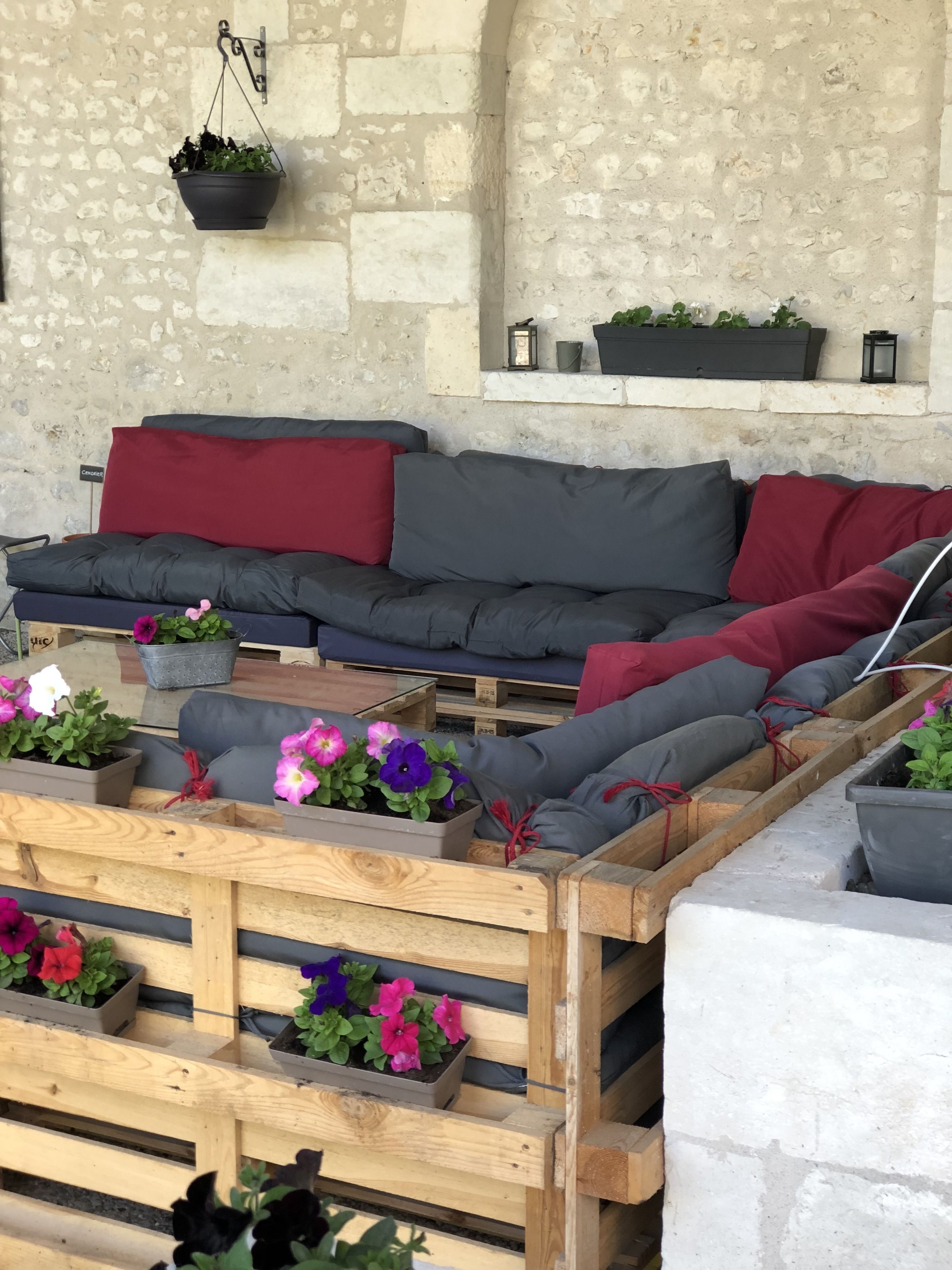 Een gezellig buitenverblijf met een comfortabele bank, houten plantenbakken met bloemen en een hangplant.