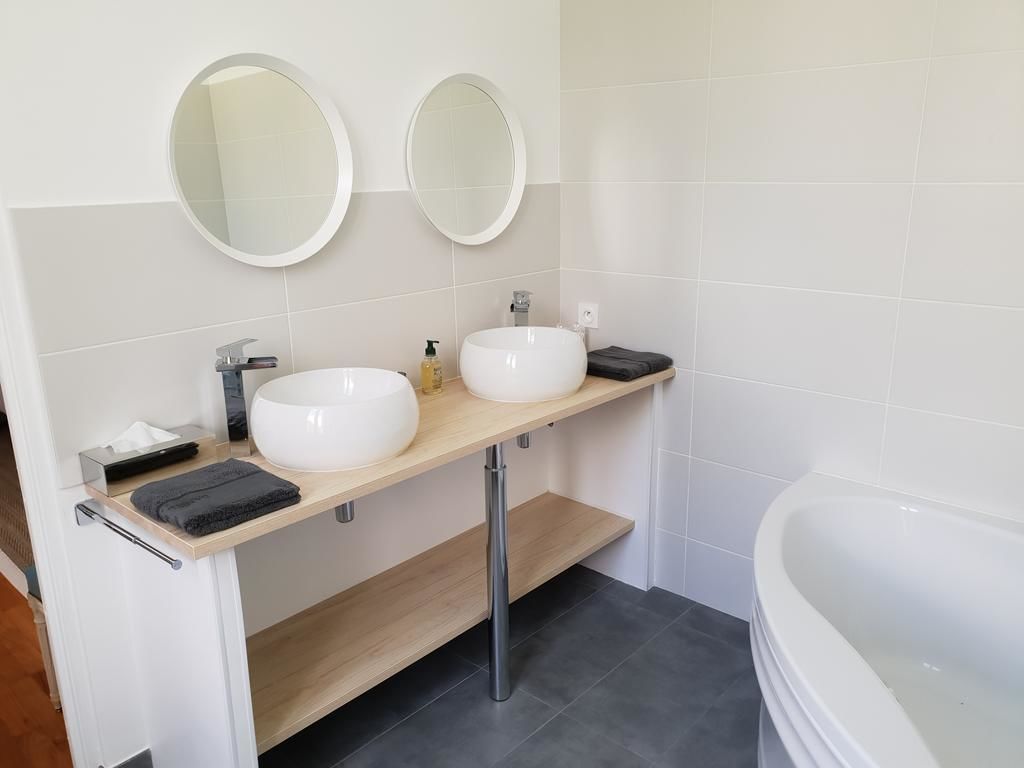 Un baño moderno con dos lavamanos blancos, un mueble de tocador de madera, un espejo grande y una bañera blanca.