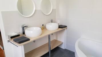 Un baño moderno con dos lavamanos blancos, un mueble de tocador de madera, un espejo grande y una bañera blanca.
