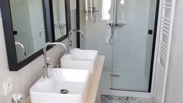 Un baño moderno con tres lavamanos blancos, un espejo grande y una cabina de ducha de vidrio.