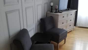 A room with a wooden floor, a white dresser with drawers, a television on top, and two dark-colored chairs.