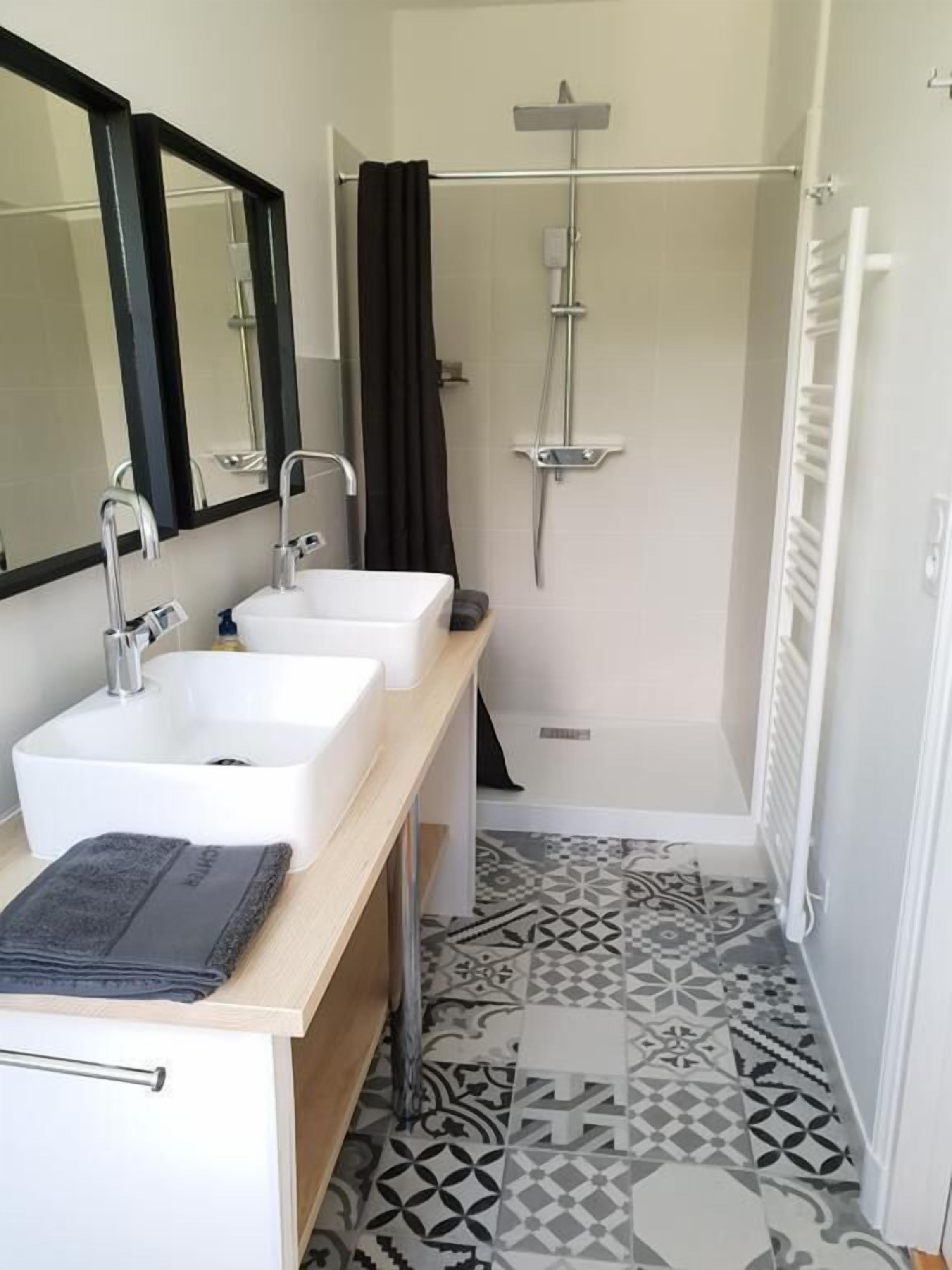A bathroom with two sinks, a shower, and a patterned floor.