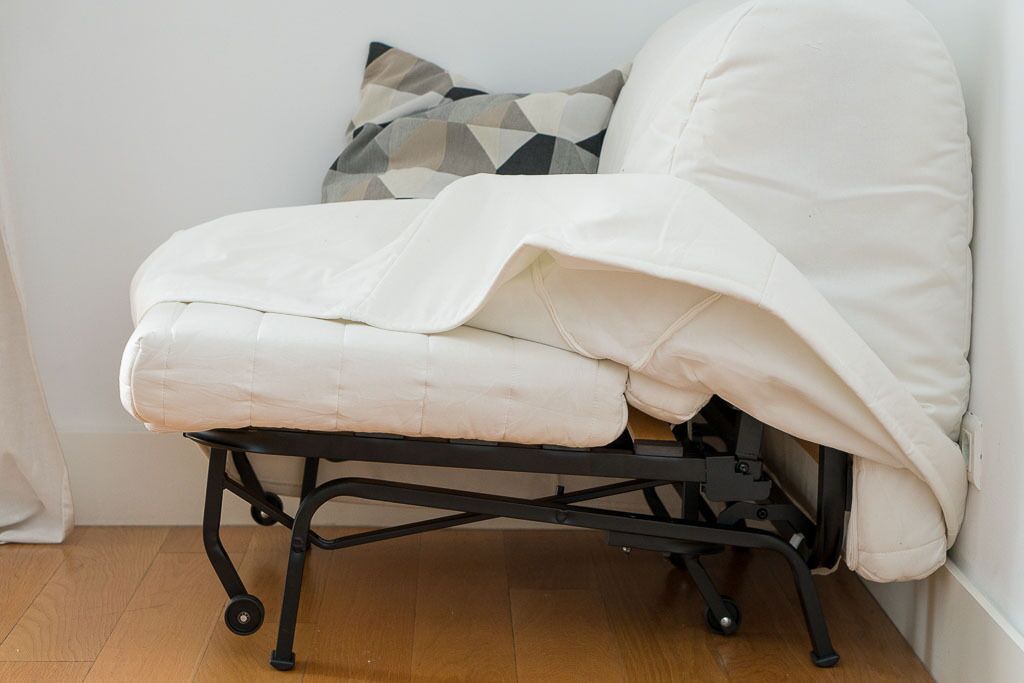 Ein Ecksofa mit weißem Bezug, schwarzem Metallgestell und einem grauen Kissen mit schwarzem Muster.