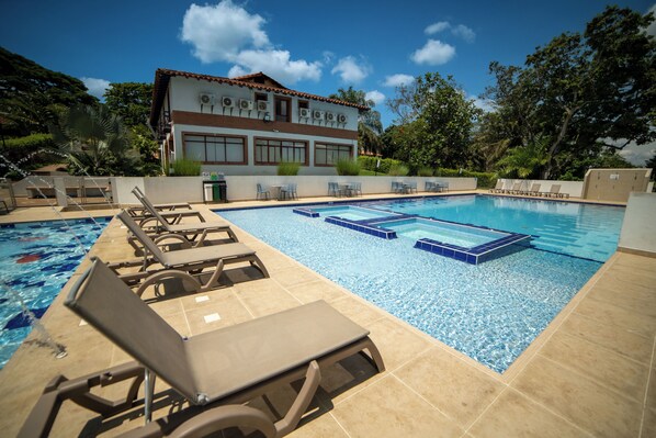 A swimming pool with lounge chairs and a building in the background. - Hotel Barranqueros (Armenia)