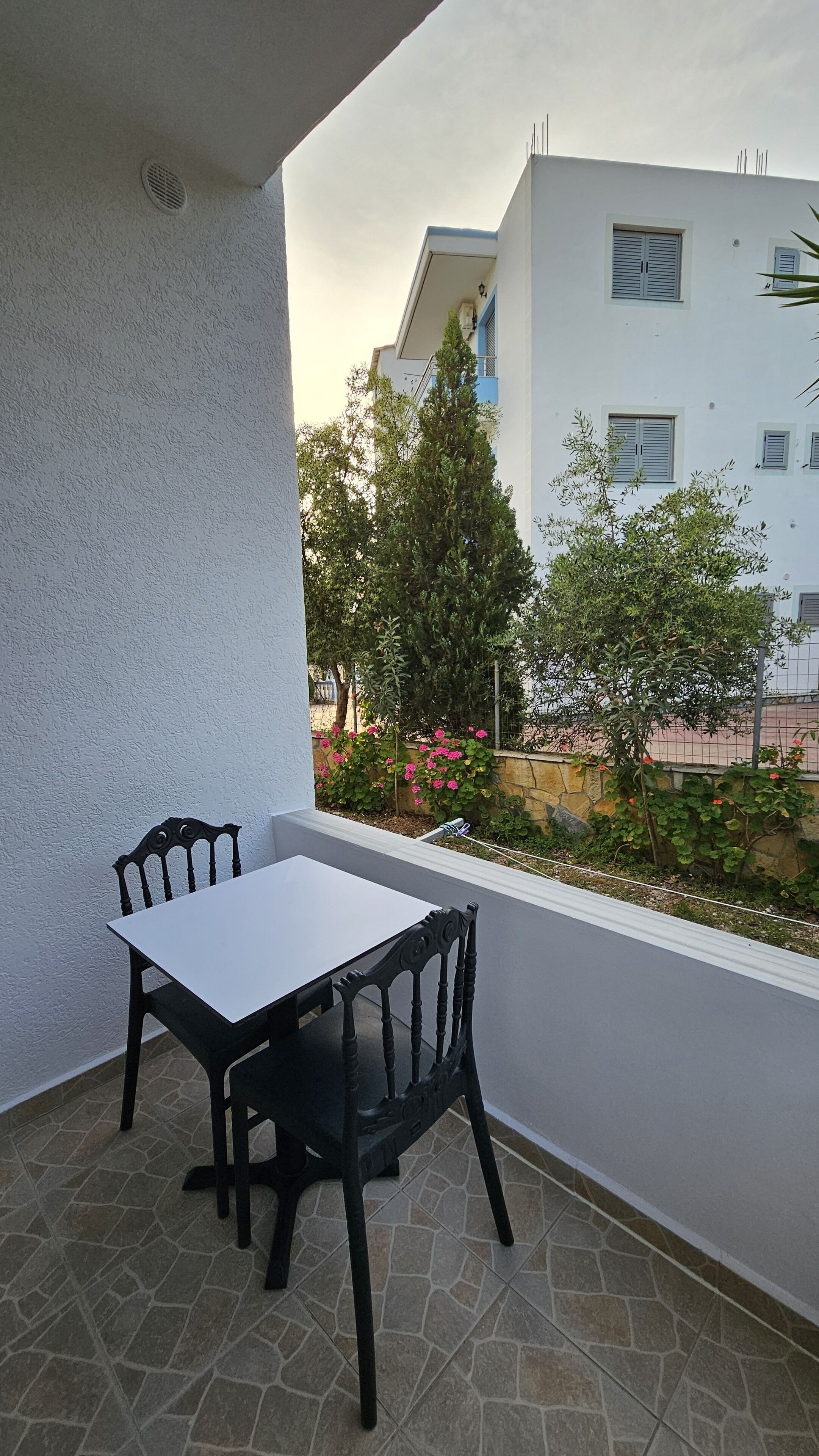 Un balcon avec une table et des chaises, une vue sur un immeuble et quelques plantes.