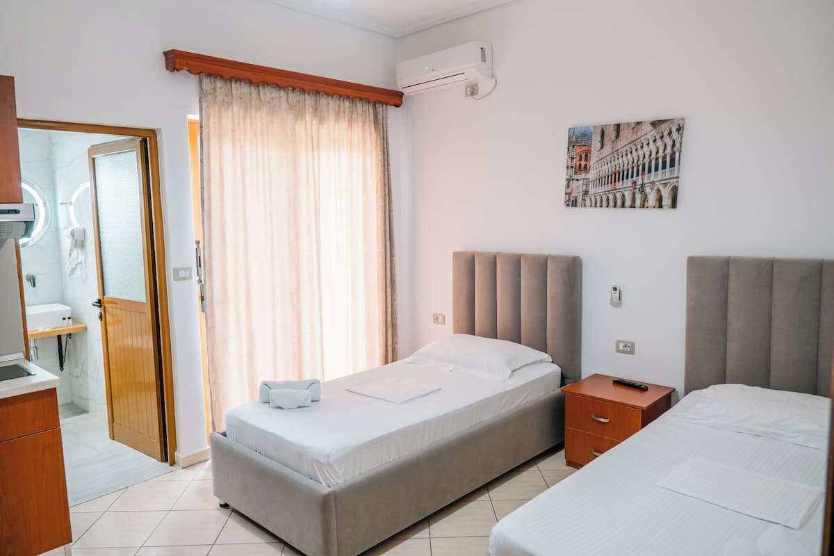 A hotel room with a bed, a bedside table, a mirror, a window with curtains, and an air conditioning unit.