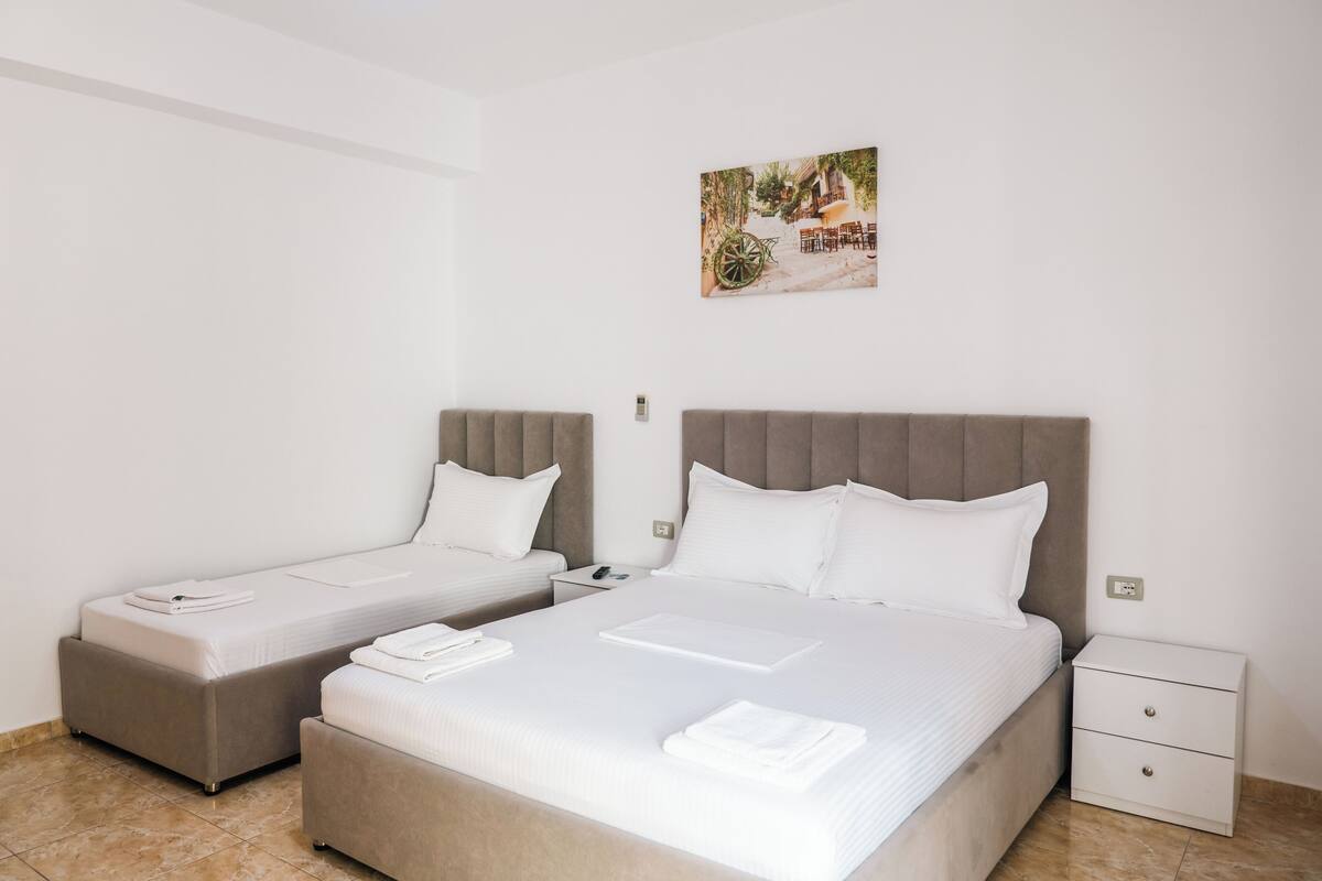 A hotel room with two beds, a nightstand, a small drawer, and a wall-mounted picture.