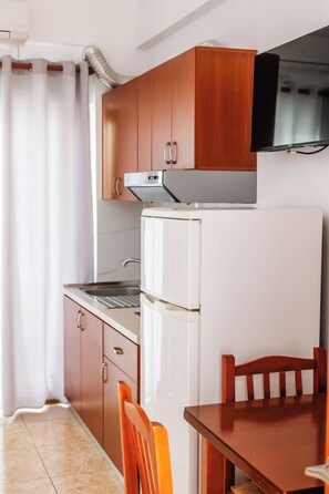 A compact kitchen with wooden cabinets, a white refrigerator, and a dining table with chairs. - Vila Malo (Ksamil)