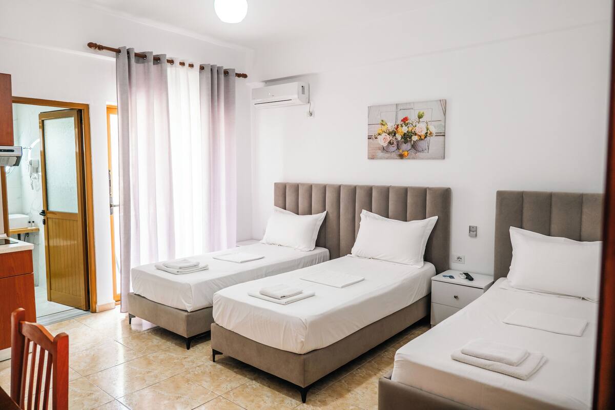 A hotel room with two beds, a bathroom, a wooden chair, and a painting on the wall.