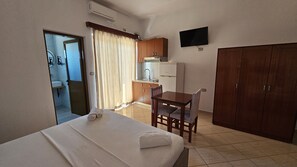 Ein Hotelzimmer mit Bett, Schreibtisch, Stuhl, Fernseher, Kleiderschrank, Küchenzeile und Badezimmer.